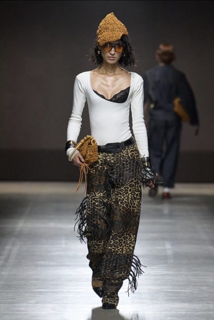 Female model walking down the runway with a scoop-neck top and printed pants. 