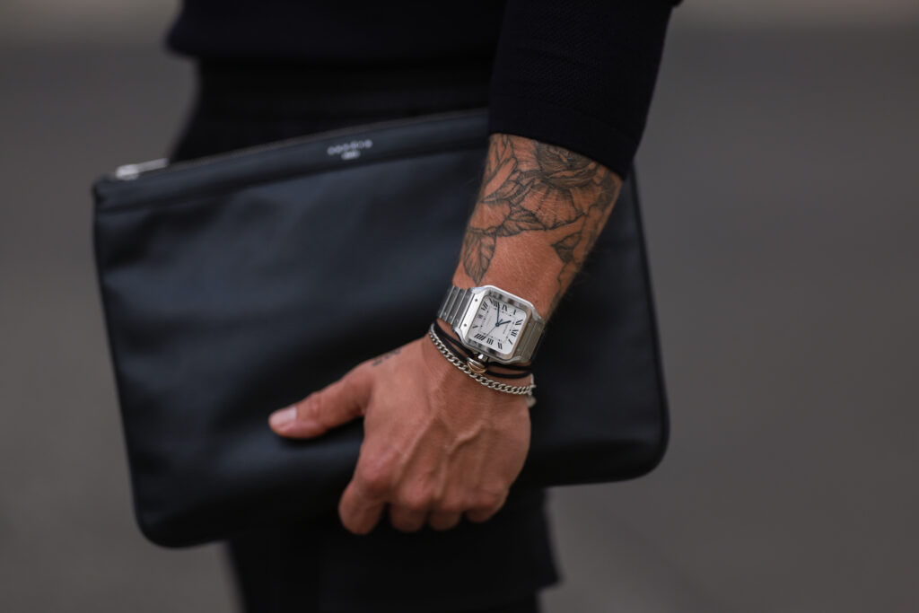 Close up of man holding a black laptop case wearing a luxury silver watch.