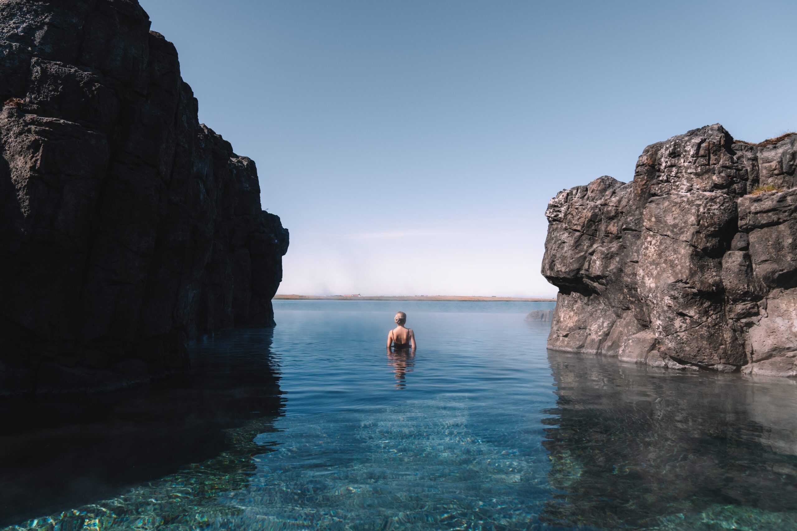 A woman swims in the clear water between two cliffs. She looks out into the distance.